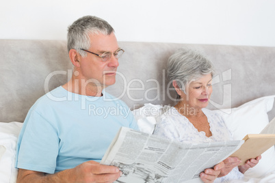 Senior couple with newspaper and book in house