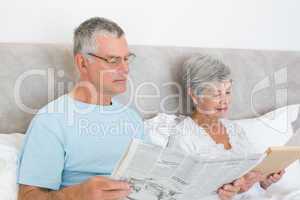 Senior couple with newspaper and book in house