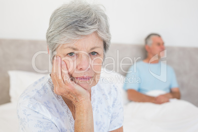 Disappointed senior woman with husband in background