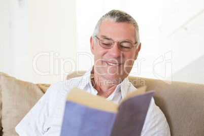 Senior man reading book on sofa