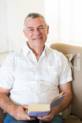 Smiling senior man holding book on sofa