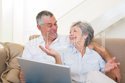 Loving senior couple with laptop on sofa