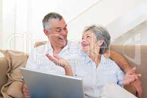 Loving senior couple with laptop on sofa