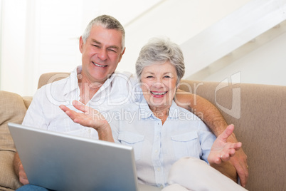 Happy senior couple with laptop on sofa