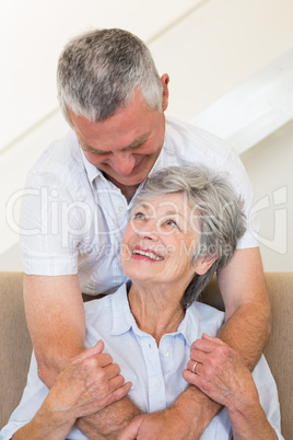 Senior man hugging wife sitting on sofa