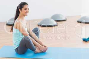Smiling fit woman doing the butterfly stretch in exercise room