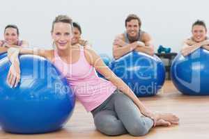 Instructor and class with exercise balls sitting at fitness stud