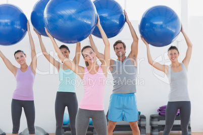 Fitness class holding up exercise balls at fitness studio