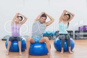 Sporty people stretching hands on exercise balls at gym