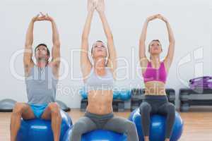 Sporty people stretching up hands on exercise balls at gym