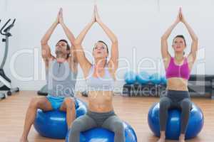 People with joined hands on exercise balls in gym