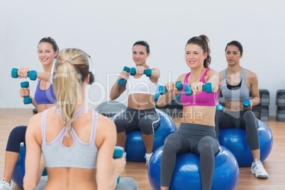 Fit class exercising with dumbbells on fitness balls