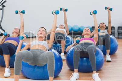 Fit class exercising with dumbbells on fitness balls