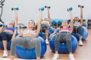 Fit class exercising with dumbbells on fitness balls