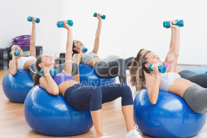 Fit class exercising with dumbbells on fitness balls