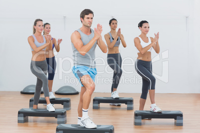 Instructor with fitness class performing step aerobics exercise