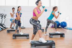 Class performing step aerobics exercise with dumbbells