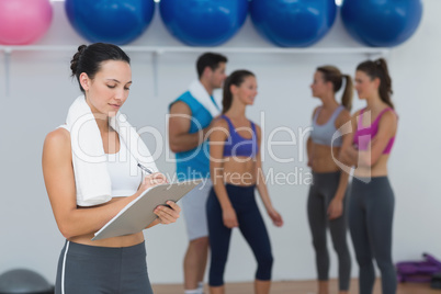 Female trainer writing on clipboard with class in background