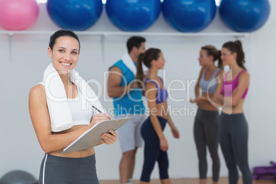 Female trainer writing on clipboard with class in background