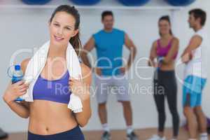 Fit female holding water bottle with fitness class in background