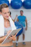 Trainer writing on clipboard with fitness class in background at