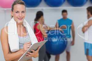 Female trainer holding clipboard with fitness class in backgroun