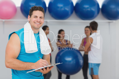 Male trainer holding clipboard with fitness class in background
