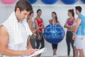 Trainer writing in clipboard with fitness class in background
