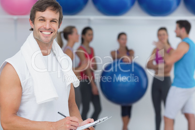 Trainer holding clipboard with fitness class in background