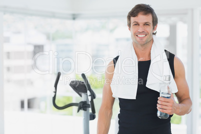 Smiling man holding water bottle at spinning class in bright gym