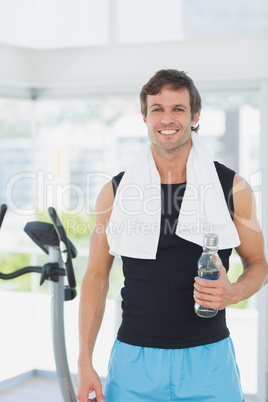 Smiling man holding water bottle at spinning class in bright gym