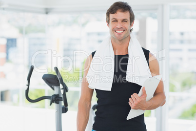 Smiling male trainer with clipboard in bright gym