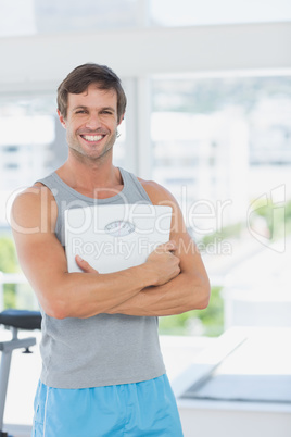 Fit man standing with scale in bright exercise room