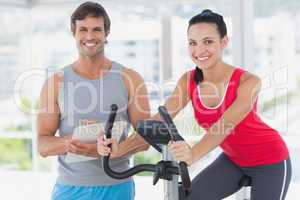 Woman with instructor working out at spinning class in bright gy