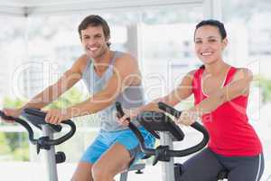 Smiling young couple working out at spinning class