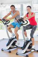 Smiling young couple working out at spinning class