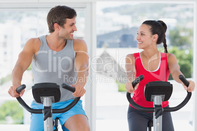 Couple working out at spinning class in bright gym