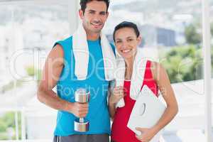 Fit couple with dumbbell and scale in bright exercise room