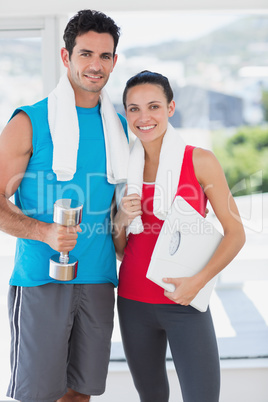 Fit couple with dumbbell and scale in bright exercise room