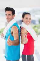 Fit couple gesturing thumbs up in bright exercise room