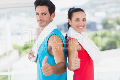 Fit couple gesturing thumbs up in bright exercise room
