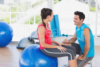 Instructor and woman with exercise ball at a bright gym