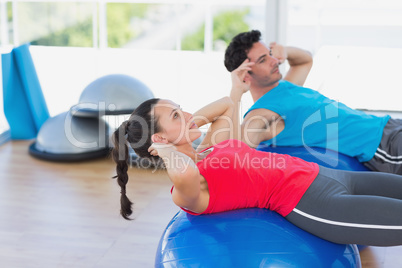 Fit young couple exercising on fitness balls at gym