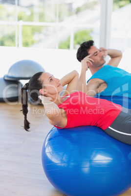 Fit couple exercising on fitness balls at gym