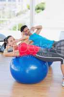 Fit young couple exercising on fitness balls at gym