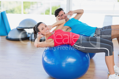 Fit young couple exercising on fitness balls at gym