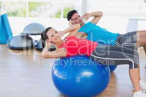Fit young couple exercising on fitness balls at gym
