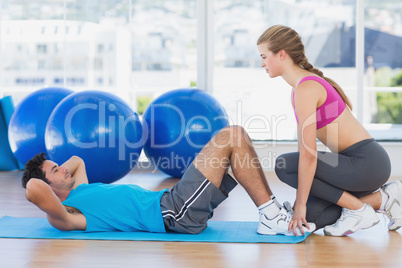 Female trainer helping man with his exercises at gym