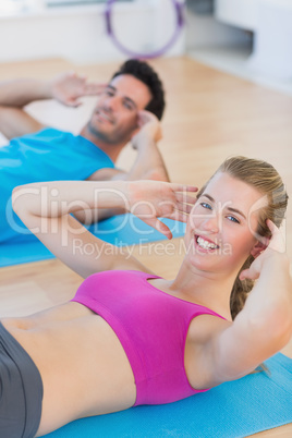 Smiling young couple doing sit ups at gym