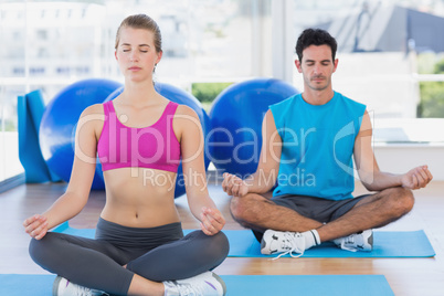 Couple sitting in lotus posture and eyes closed at fitness studi
